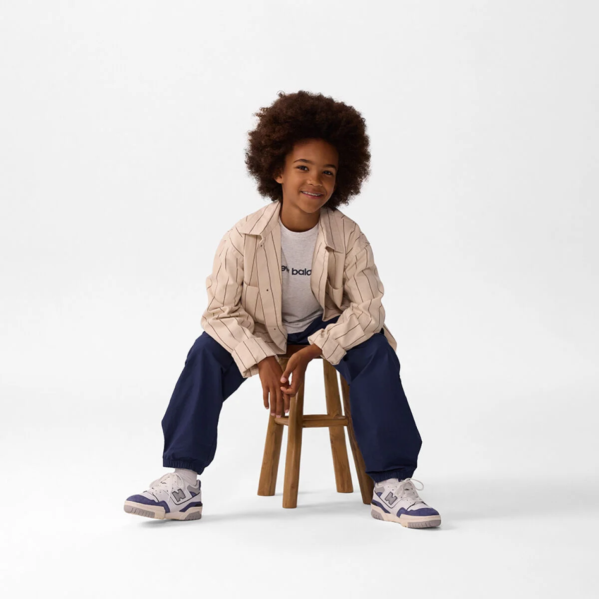 Young kid sitting on a stool wearing blue pants. 