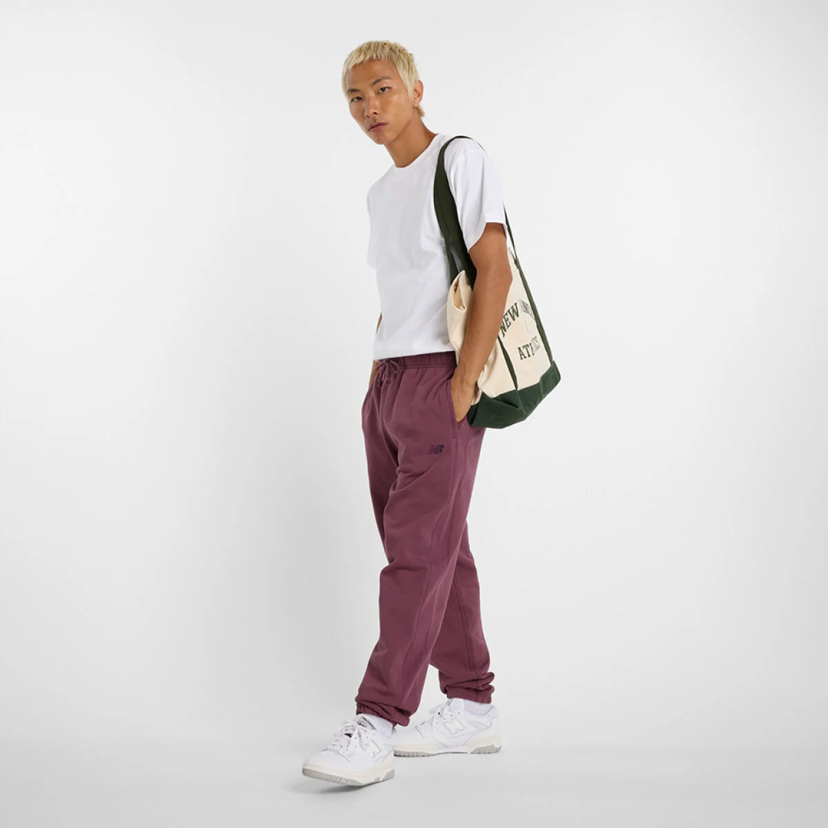 Young man in maroon pants holding a NB Bag over his shoulder. 